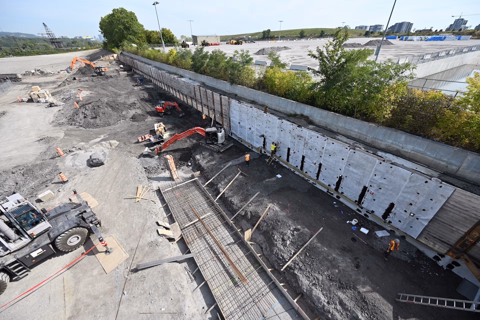 Construction site with workers, machinery, and a retaining wall insulated with white panels.